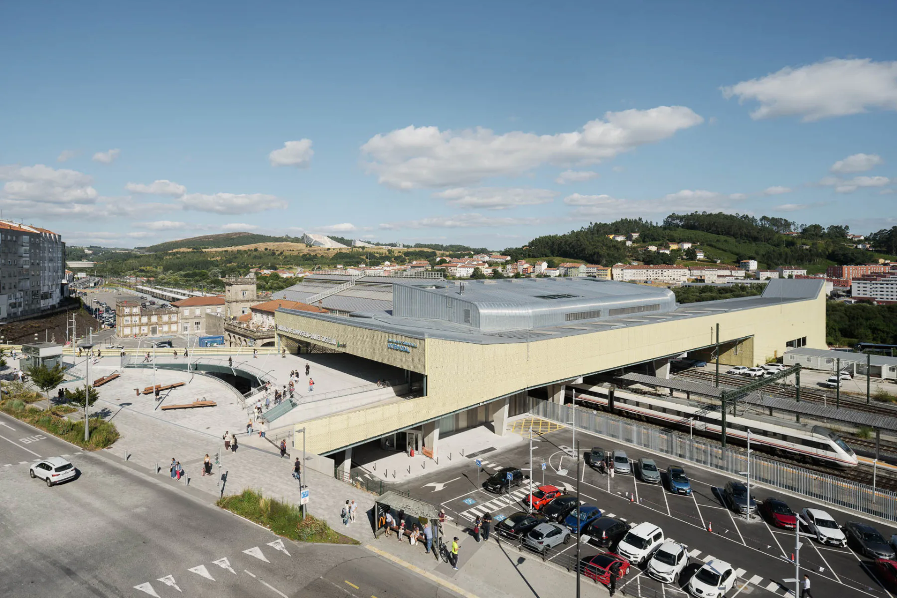 Gesamtansicht des neuen Bahnhofsgebäudes von Westen. Im Hintergrund links ist das alte Empfangsgebäude zu sehen, darüber im Hintergrund die Ciudad de la Cultura.