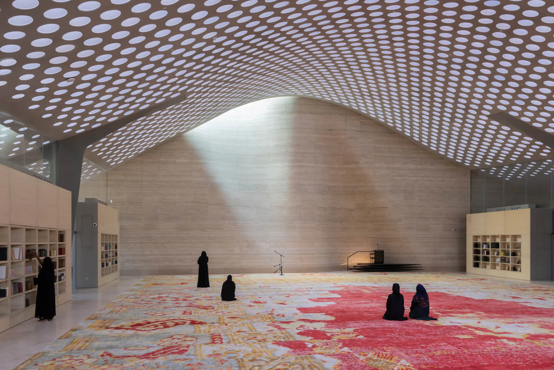 Blick in die Frauenmoschee im Bildungszentrum Al Mujadilah Center in Doha: Die nach Mekka gerichtete Quibla-Wand mit Travertinbekleidung ist am höchsten Punkt in Raummitte nach außen gewellt und bildet eine Mihrab-Gebetsnische.