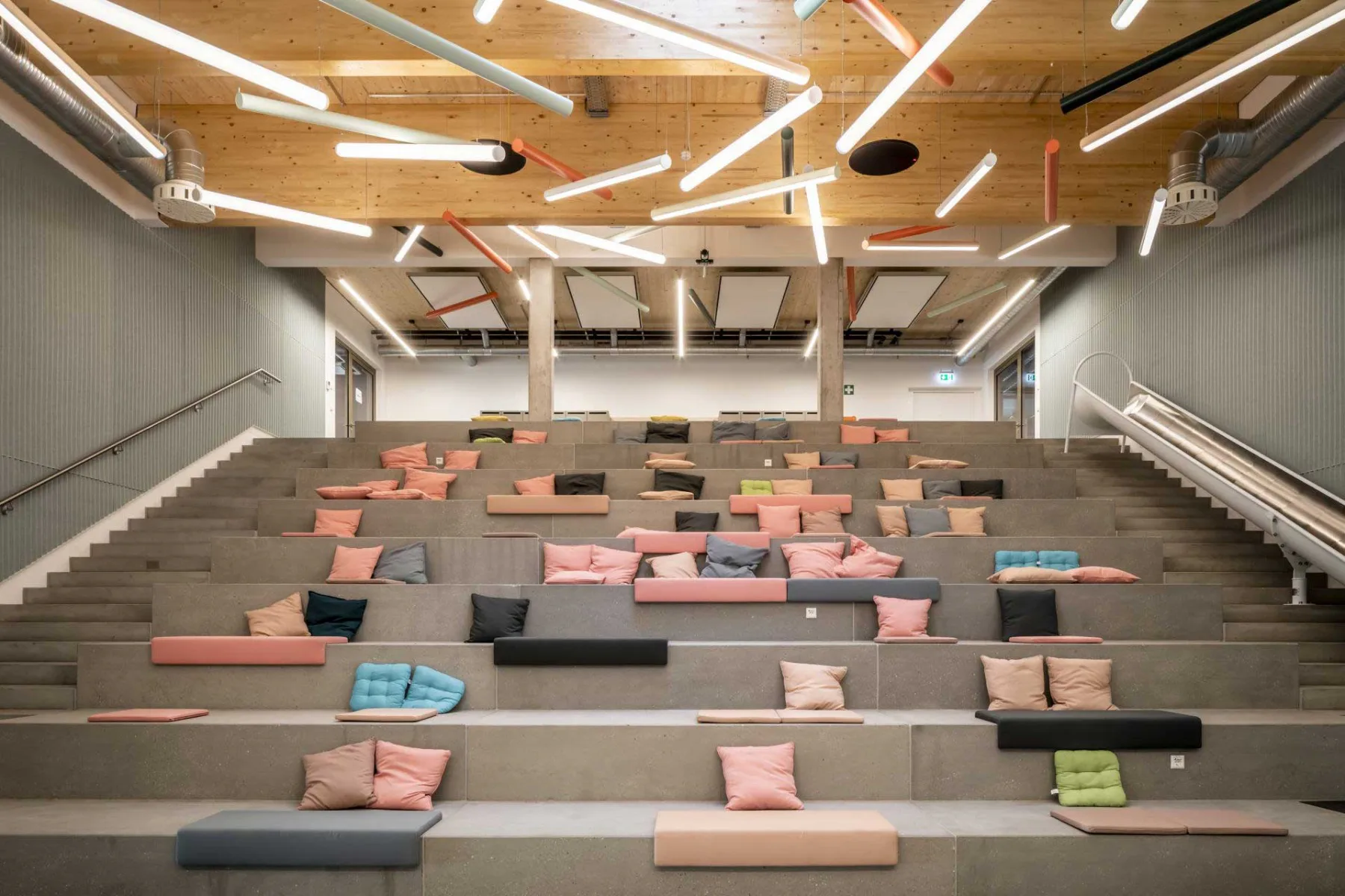 Statt klassischen Büroarbeitsplätzen liegt der Fokus auf kreativen Gemeinschaftsflächen, wie einem großzügigen Atrium mit Sitztreppe und Rutsche sowie großer Leinwand.