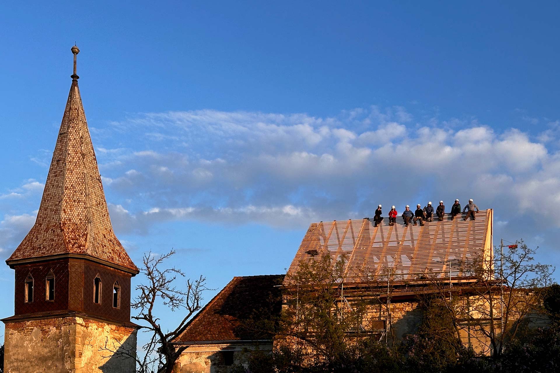 Freiwillige beobachten den Sonnenuntergang auf dem neu restaurierten Dach der Wehrkirche von Vermeș / Ambulance for Monuments
