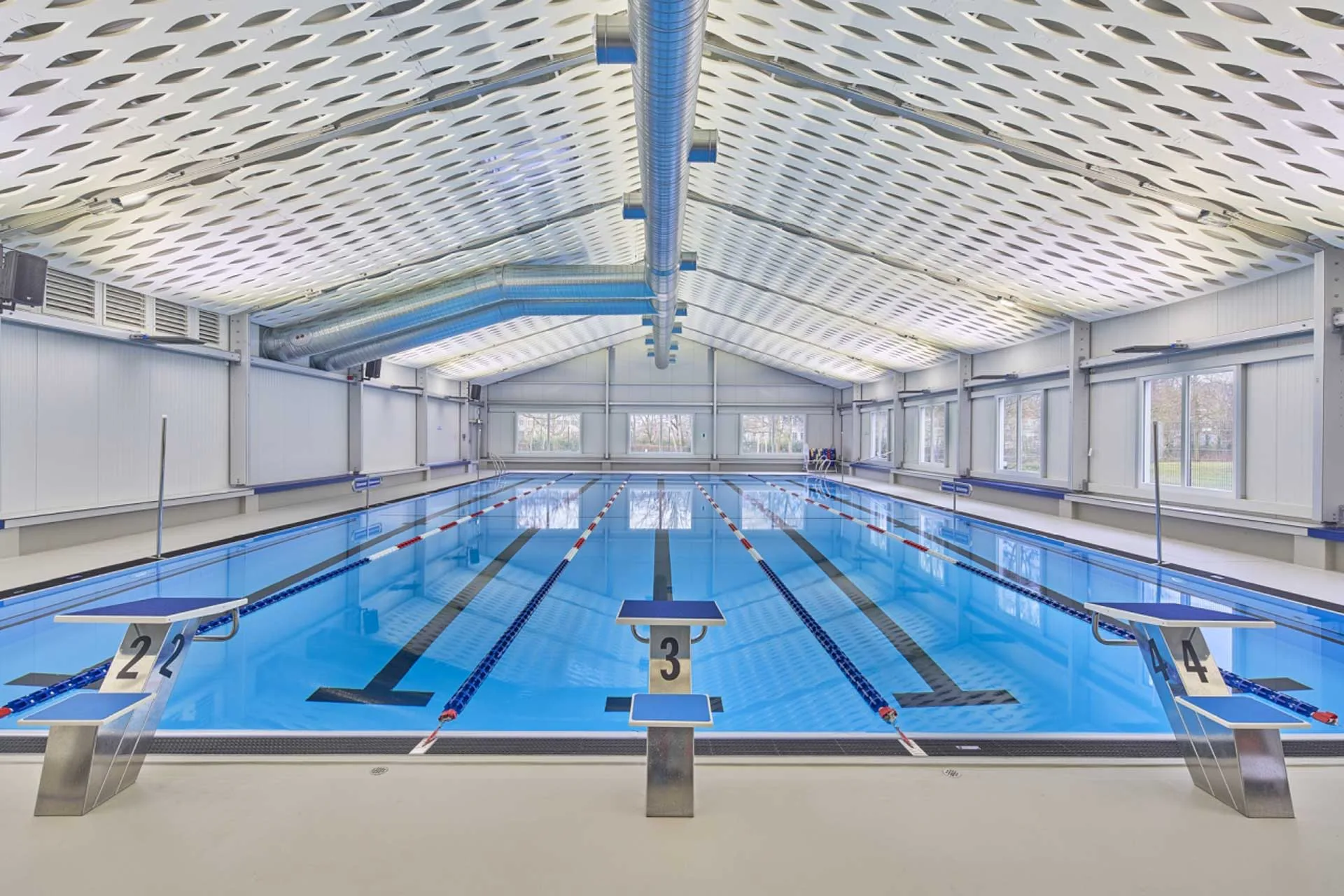 Schwimmhalle mit Akustikdecke sowie sichtbarer Tragkonstruktion und Haustechnik.
