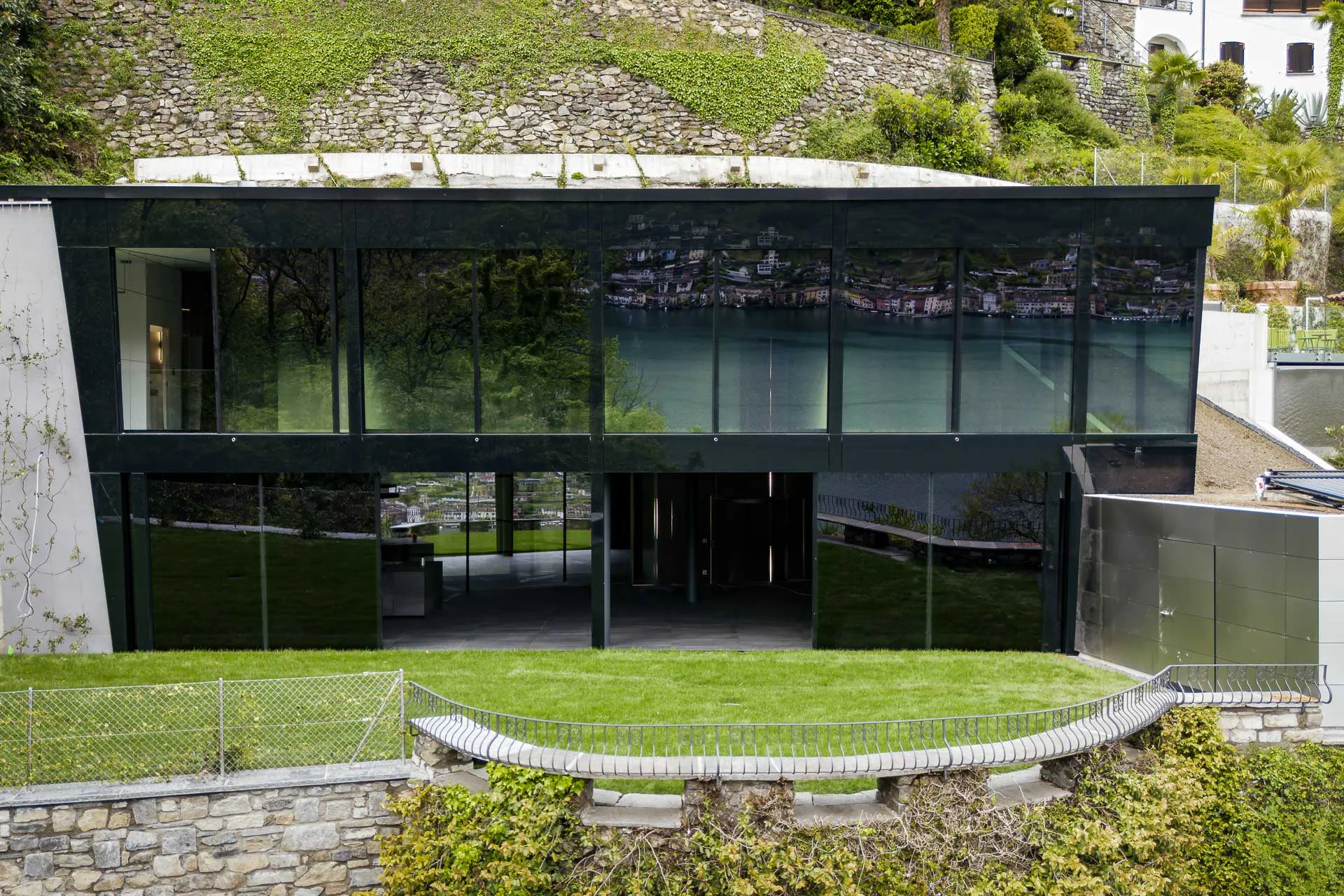 Oberhalb des Lago di Lugano haben DeltaZero Architekten ein monolitisches Ferienhaus mit einer durchgängig elektrochrom verglasten Süd-Ost-Fassade errichtet.