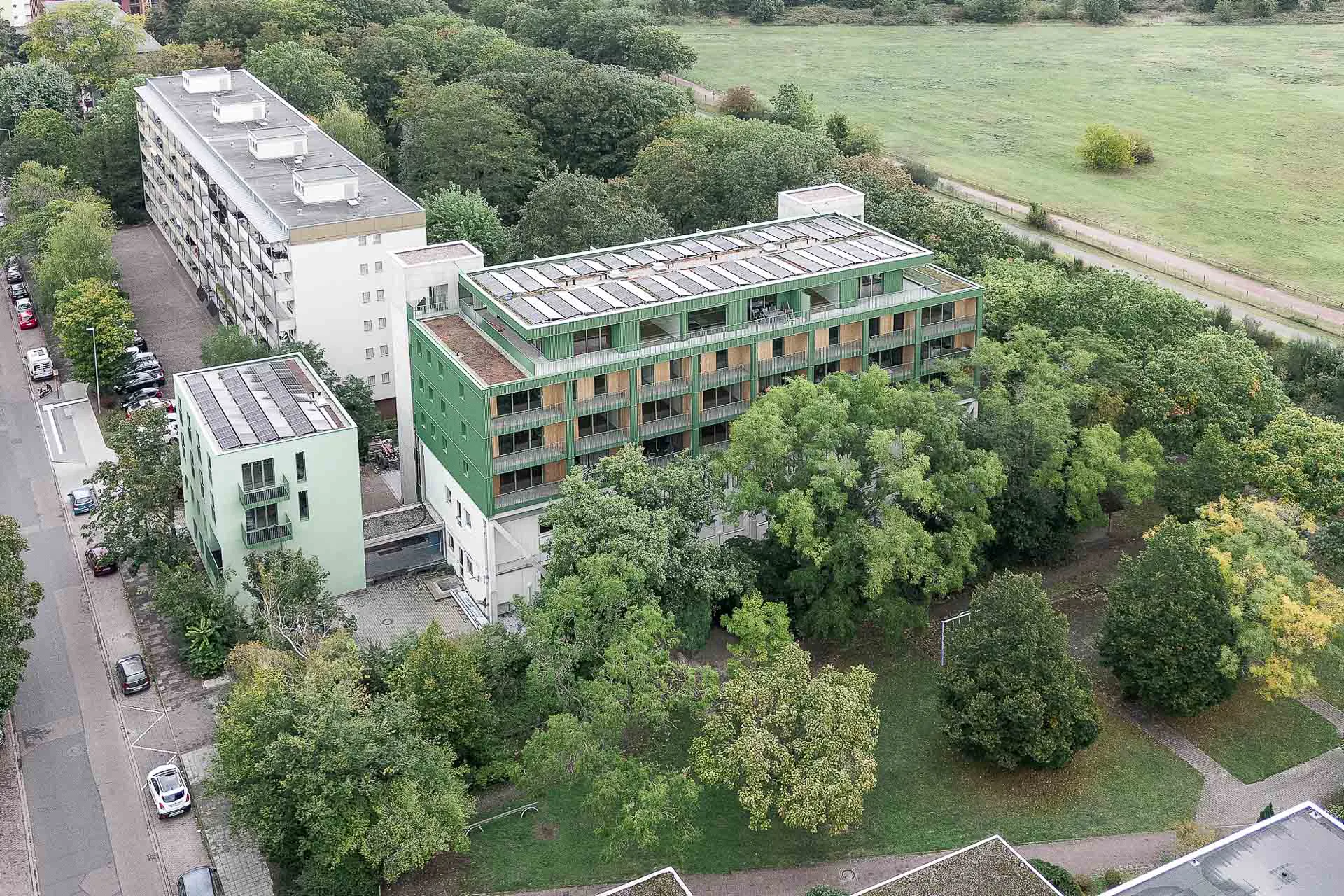Das Luftbild von Süden zeigt das zweiteilige Gebäudeensemble. Rechts im Hintergrund der ehemalige Karlsruher Flugplatz. Davor verläuft in einem Geländeeinschnitt die S-Bahn.