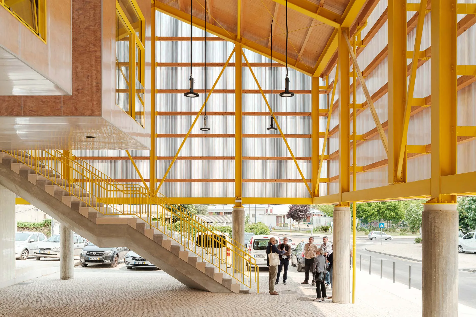 Transluzente Doppelfassade aus wiederverwendbaren Polycarbonatplatten vor gelblackierten Stahl-Portalrahmen, ausgesteift durch eine Holzpfette, die das übergroße Dach trägt.