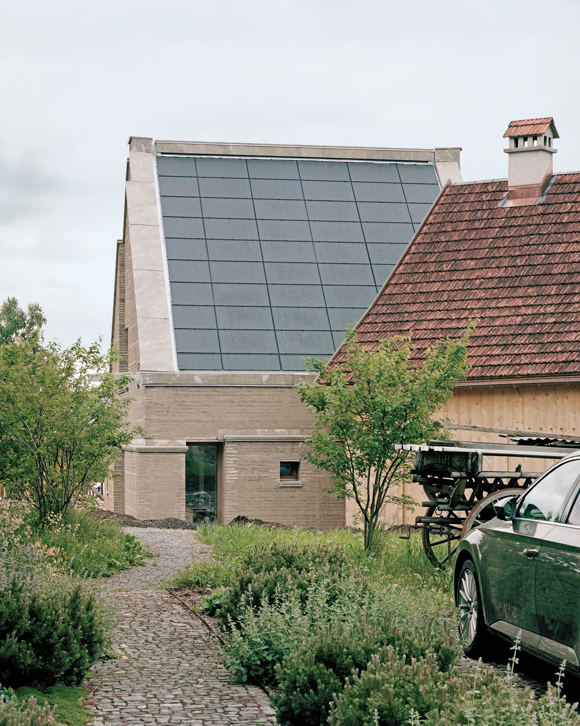 Das Dach des neuen Anbaus ist vollflächig mit Photovoltaik-Modulen belegt (links). Eine Schiebetür verbindet den Stampflehmbau mit dem historischen Strickbau.