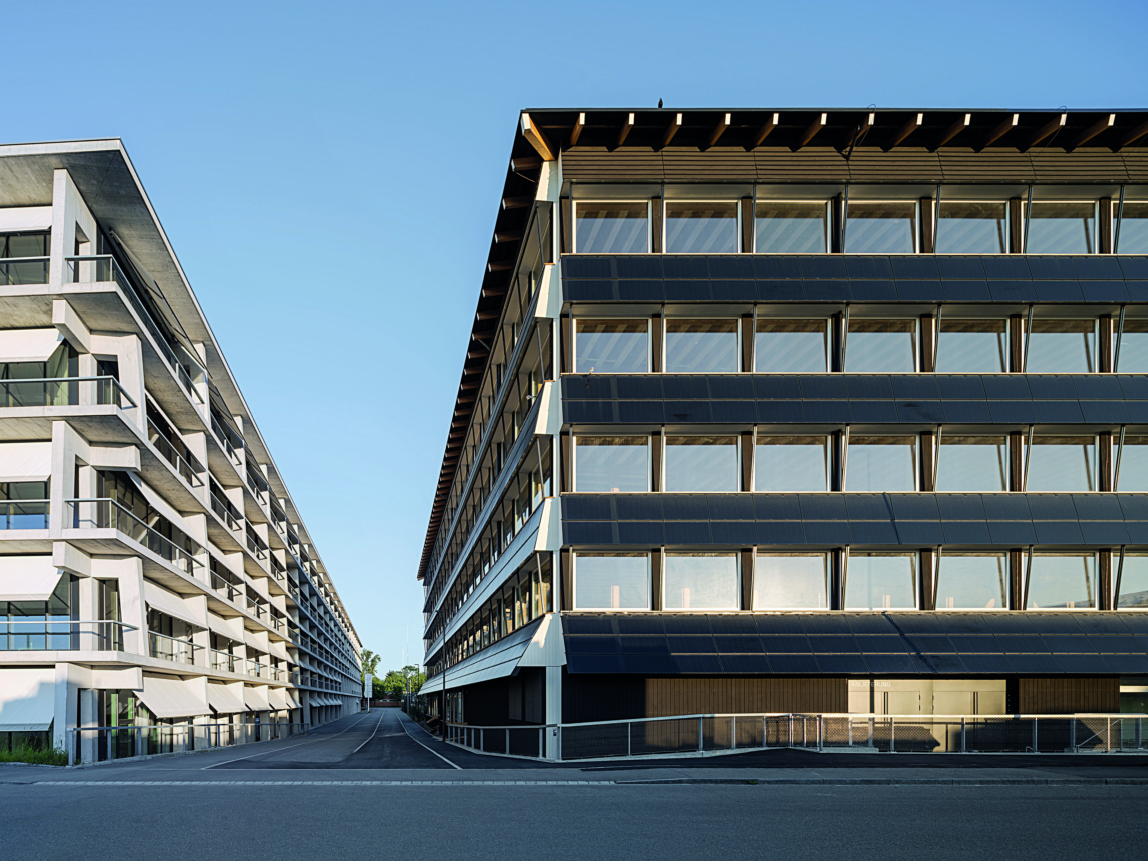 Photovoltaik Module prägen die Fassade. Die schwarzen Bänder stehen im Kontrast zu den weißen Holz fenstern und dem textilem Sonnenschutz.
