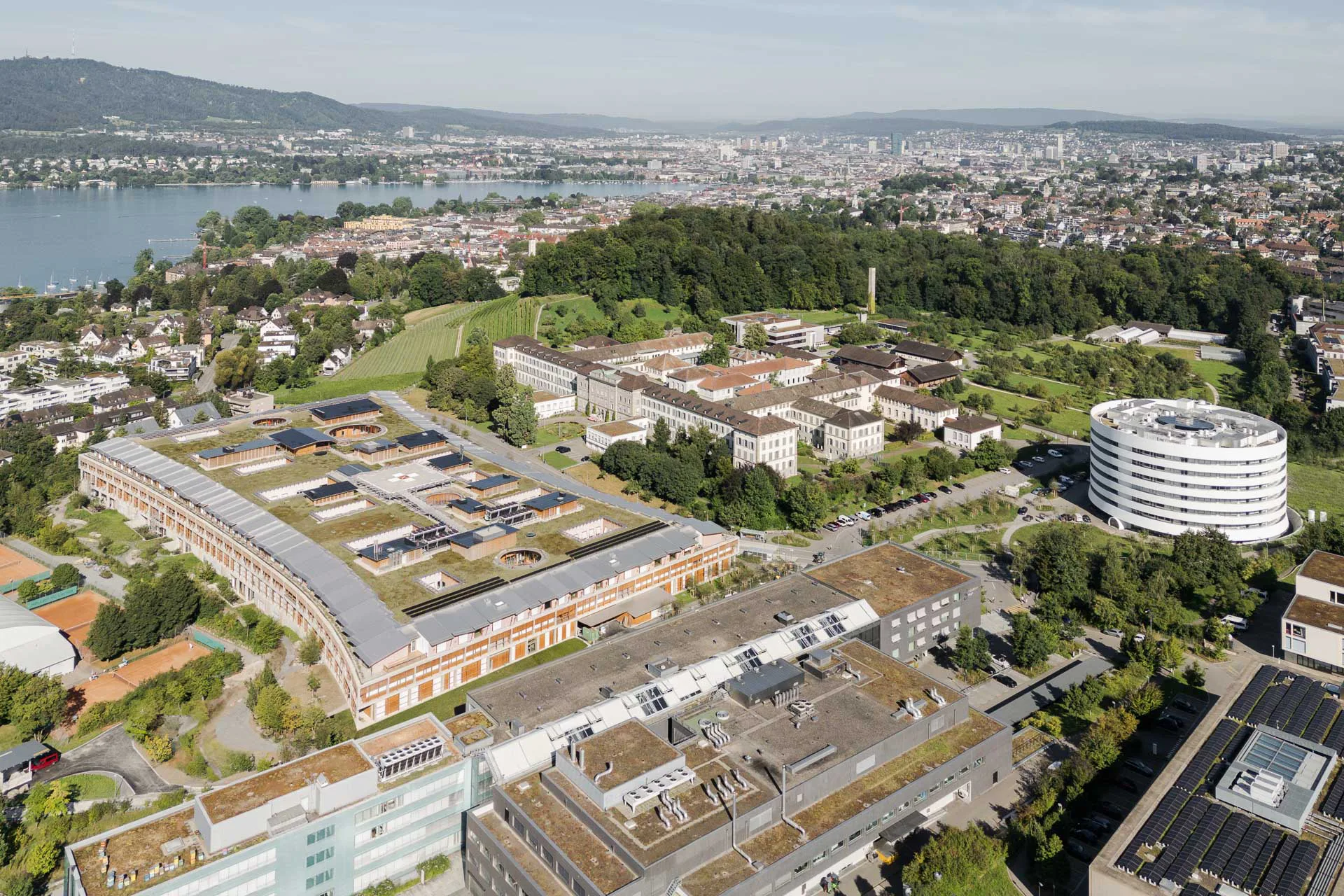 Forschungs- und Klinikbetrieb sind voneinander getrennt. Rechts erhebt sich der weiße, zylindrische Forschungsturm, links schmiegt sich das Akutspital in seine grüne Umgebung.