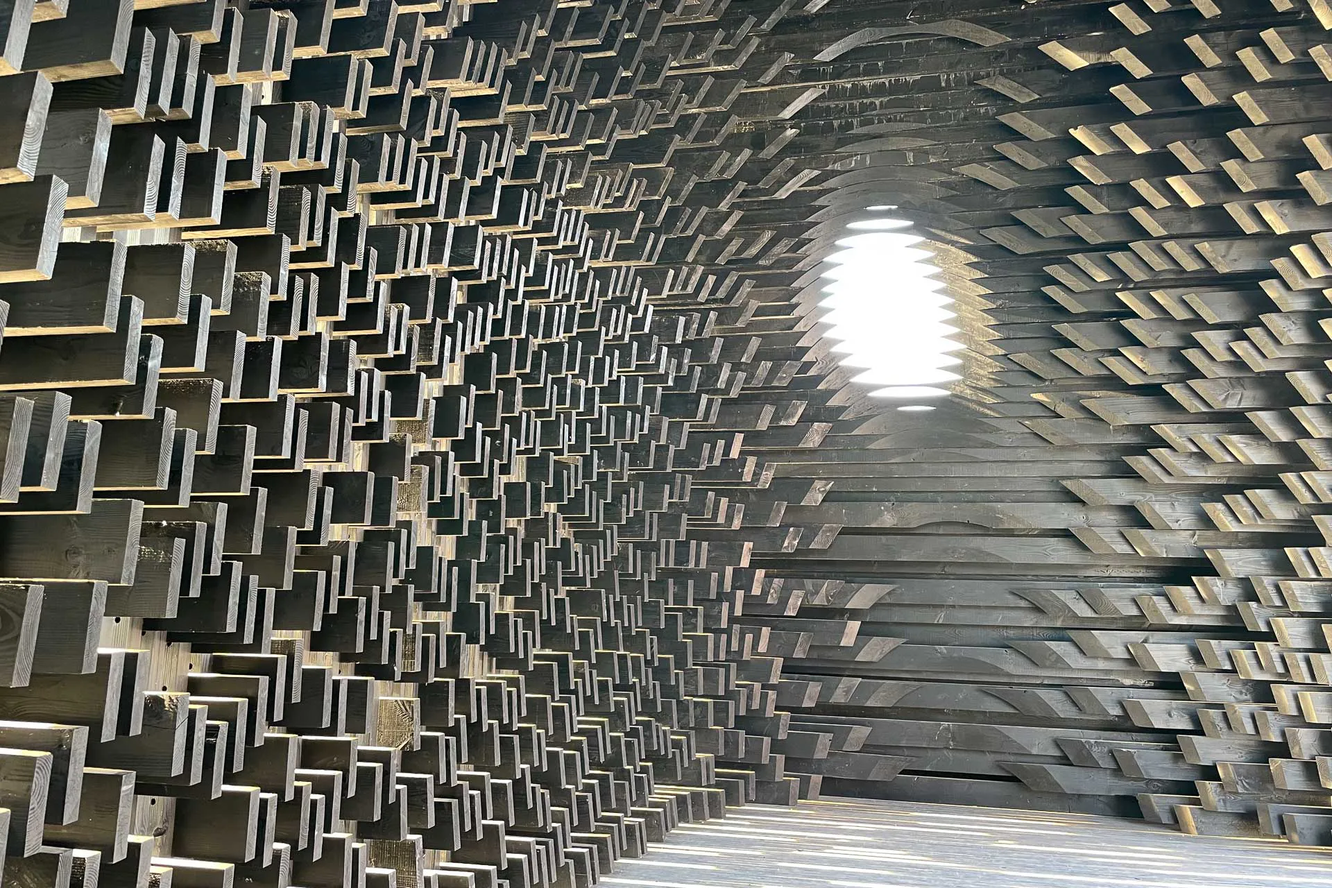 Holzbau in ungewöhnlicher Form: Zur Architekturbiennale in Venedig 2023 errichteten Adjaye Associates mit der Installation „Kwaeε“ eine begehbare, perforierte Pyramide aus geflammtem Holz.