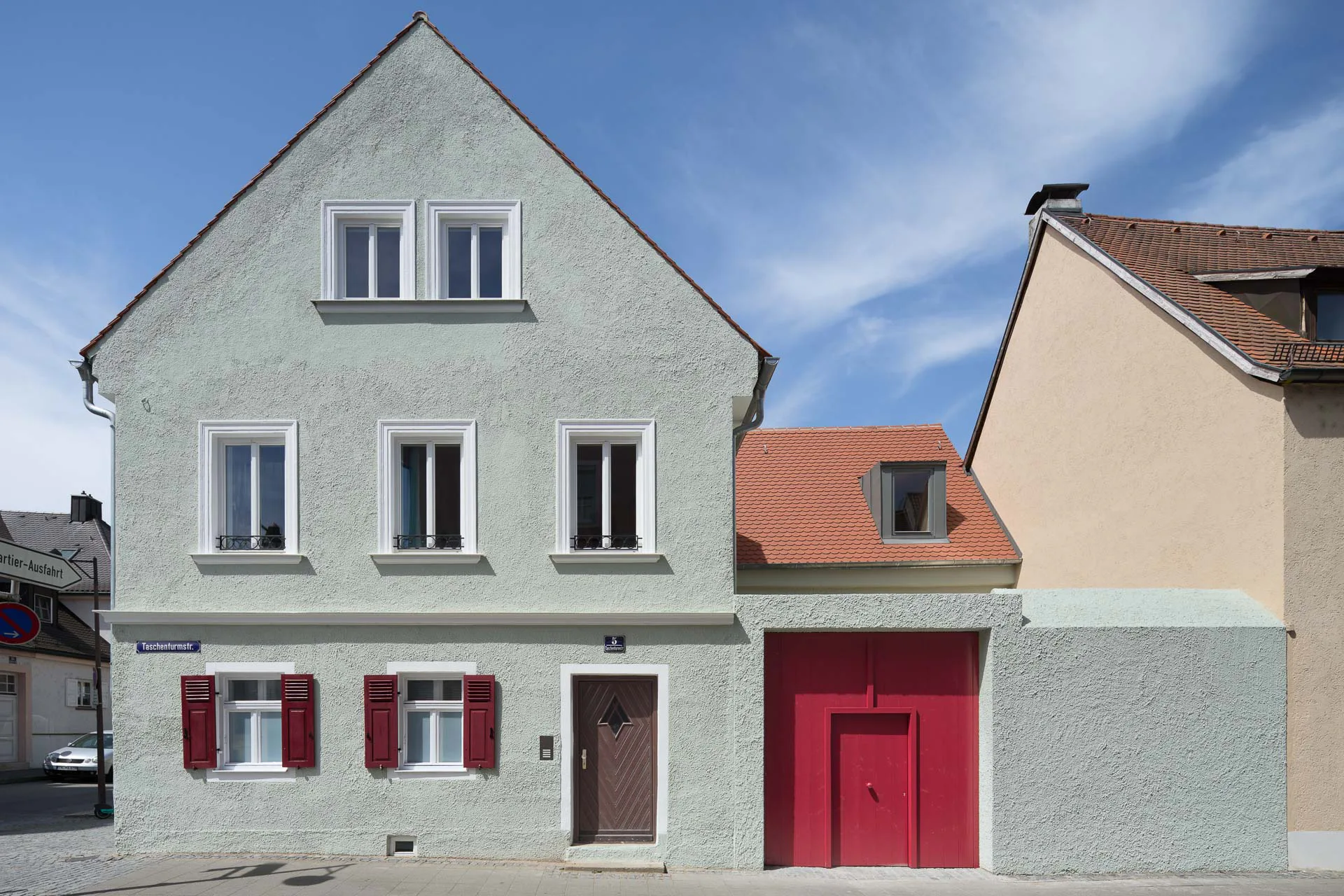 Wohnhaus, Stadel und Innenhof bleiben in ihrer Struktur klar ablesbar; die präzise gesetzten Eingriffe treten zurück, während das rote Tor den Übergang zum Hof selbstbewusst markiert.