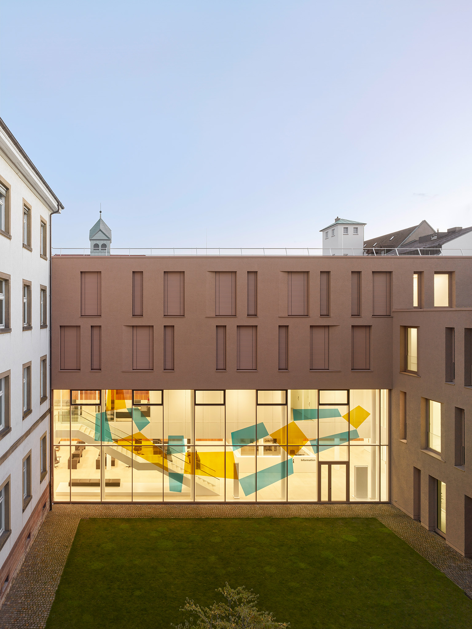 Die Nachverdichtung erforderte eine sensible Einbindung des Neubaus in die Bestandsarchitektur. Der monolithisch wirkende Baukörper mit grobkörniger Putzfassade korrespondiert perfekt mit den bestehenden Gebäuden.