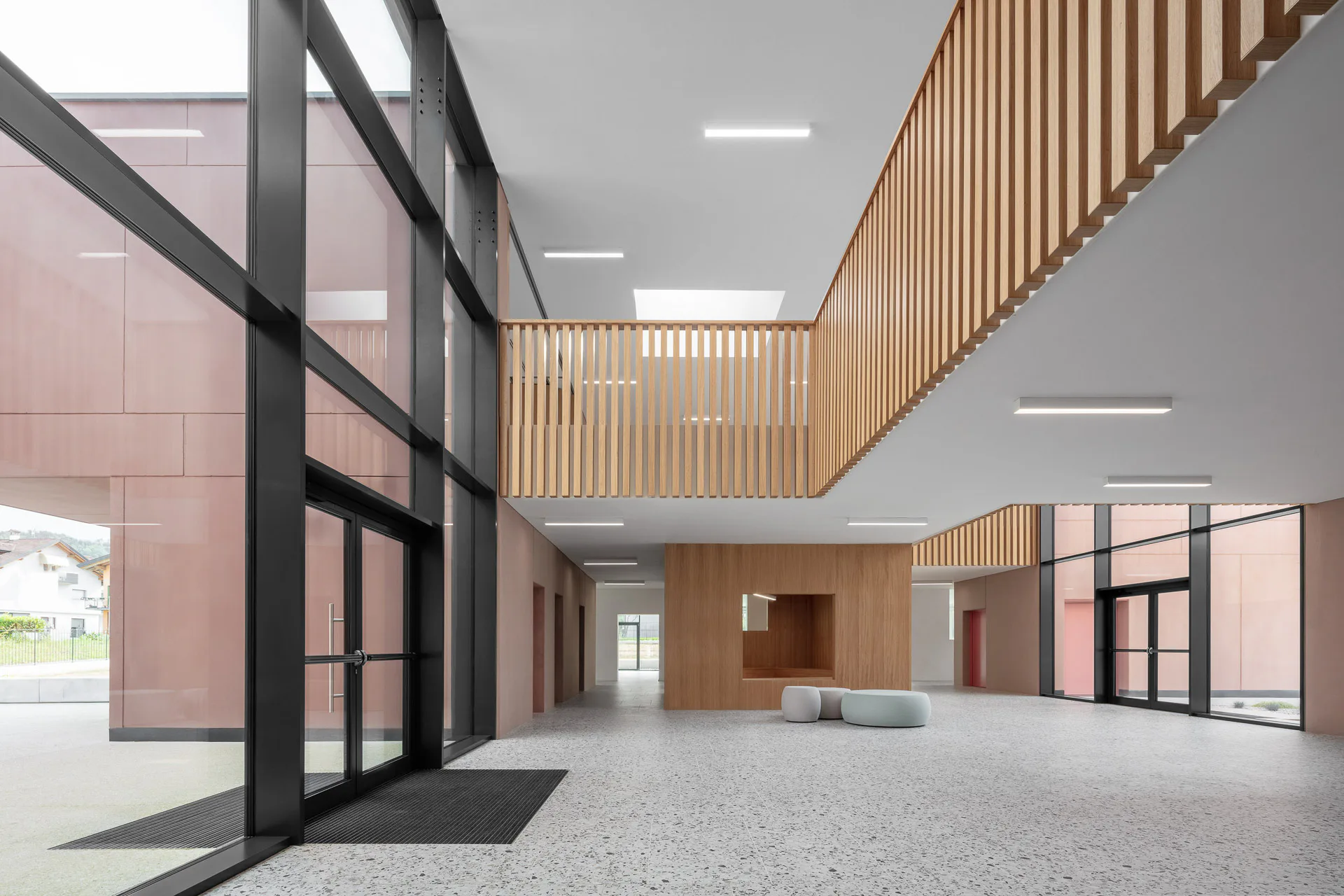Die zweigeschossige Agora der Mittelschule Puos d'Alpago, mit Terrazzoboden aus Feinsteinzeug (Le Ville, Casalgrande Padana) und Holzlamellen an der Galerie.