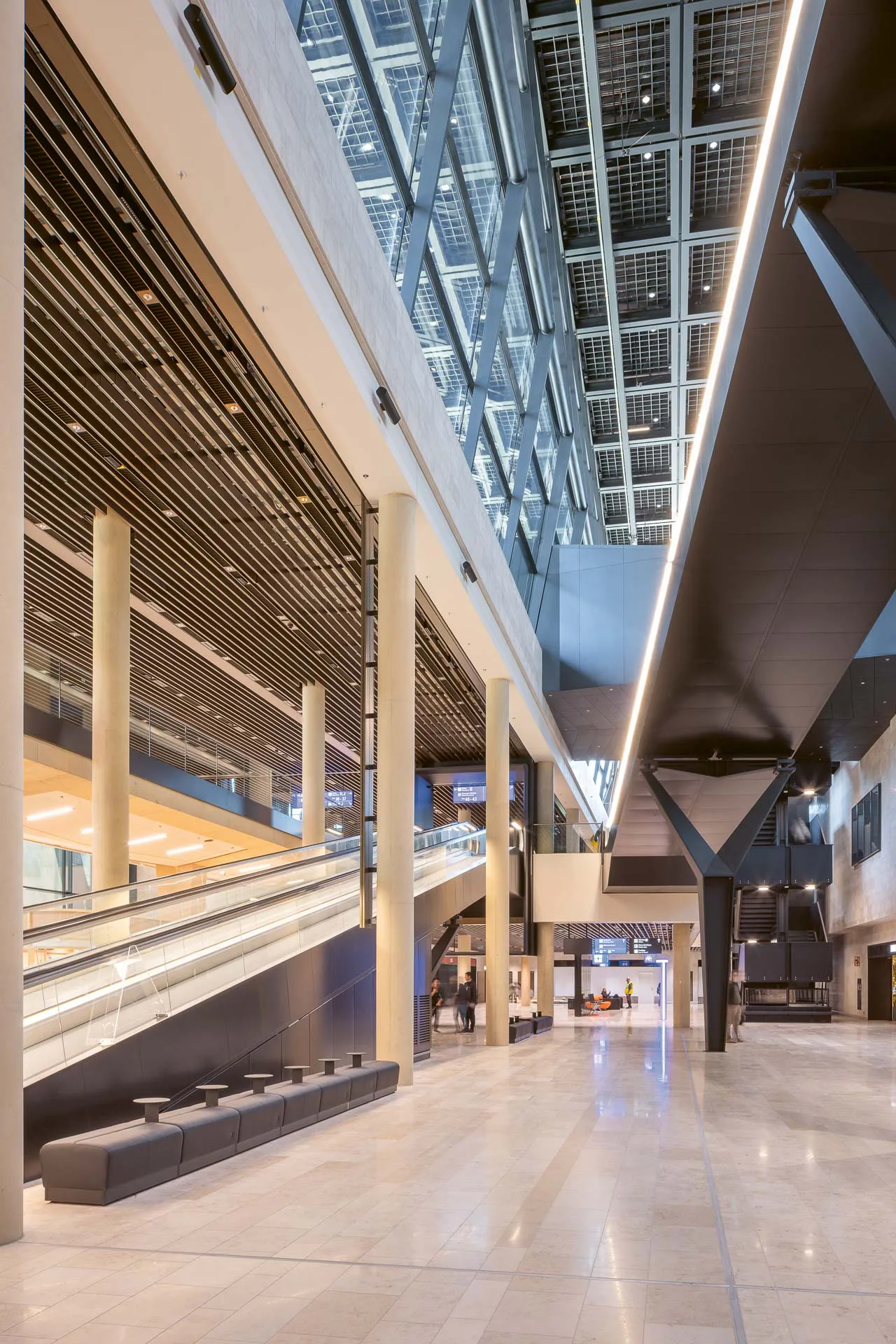 Durch den schluchtartigen Raum der Ankommerhalle mit Rollbändern und Treppen ist der signifikante Stahlrost der Abfertigungshalle bereits zu sehen.