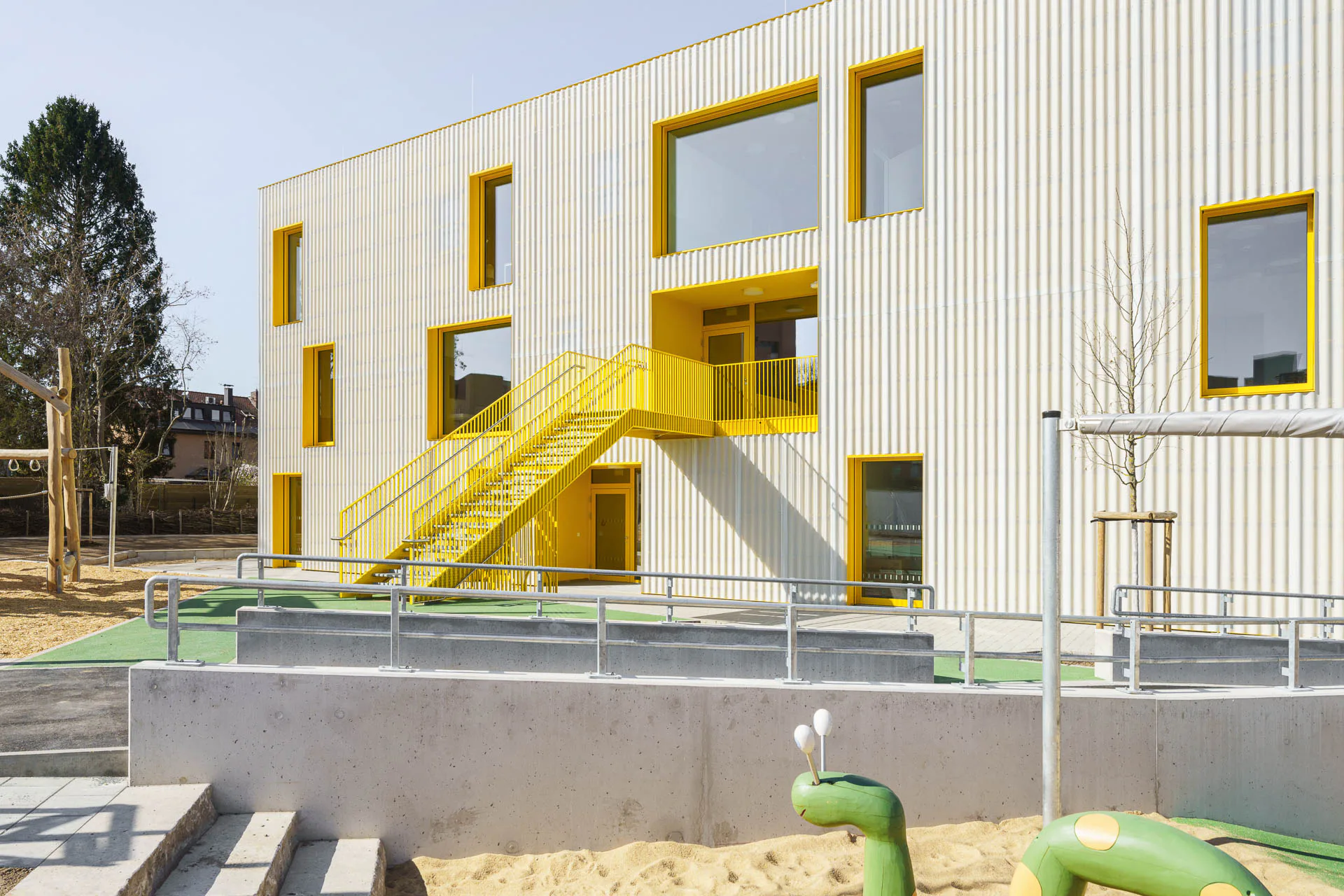 Eine knallgelbe Stahltreppe durchbricht die monolithische Gebäudehülle und führt die Vorschüler ins erste Obergeschoss.