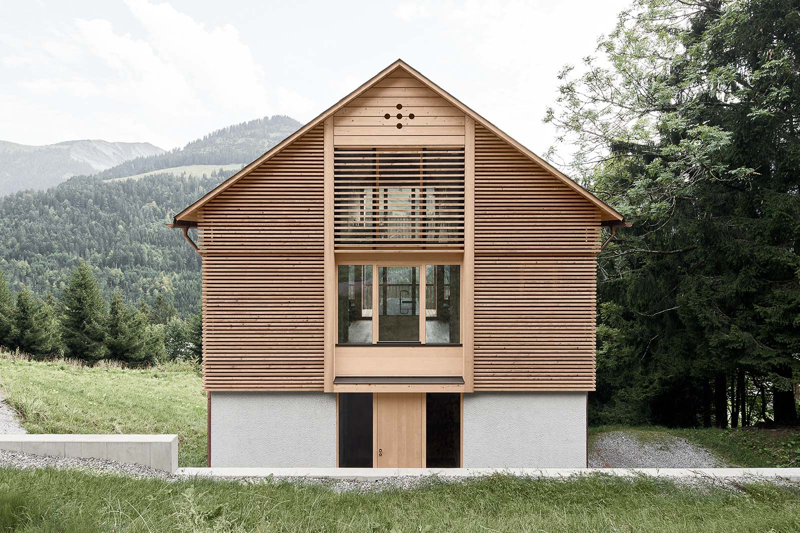 Auf dem massiven Betonsockel sitzt der hölzerne Aufbau inmitten der grünen Berglandschaft des Bregenzerwaldgebirges.