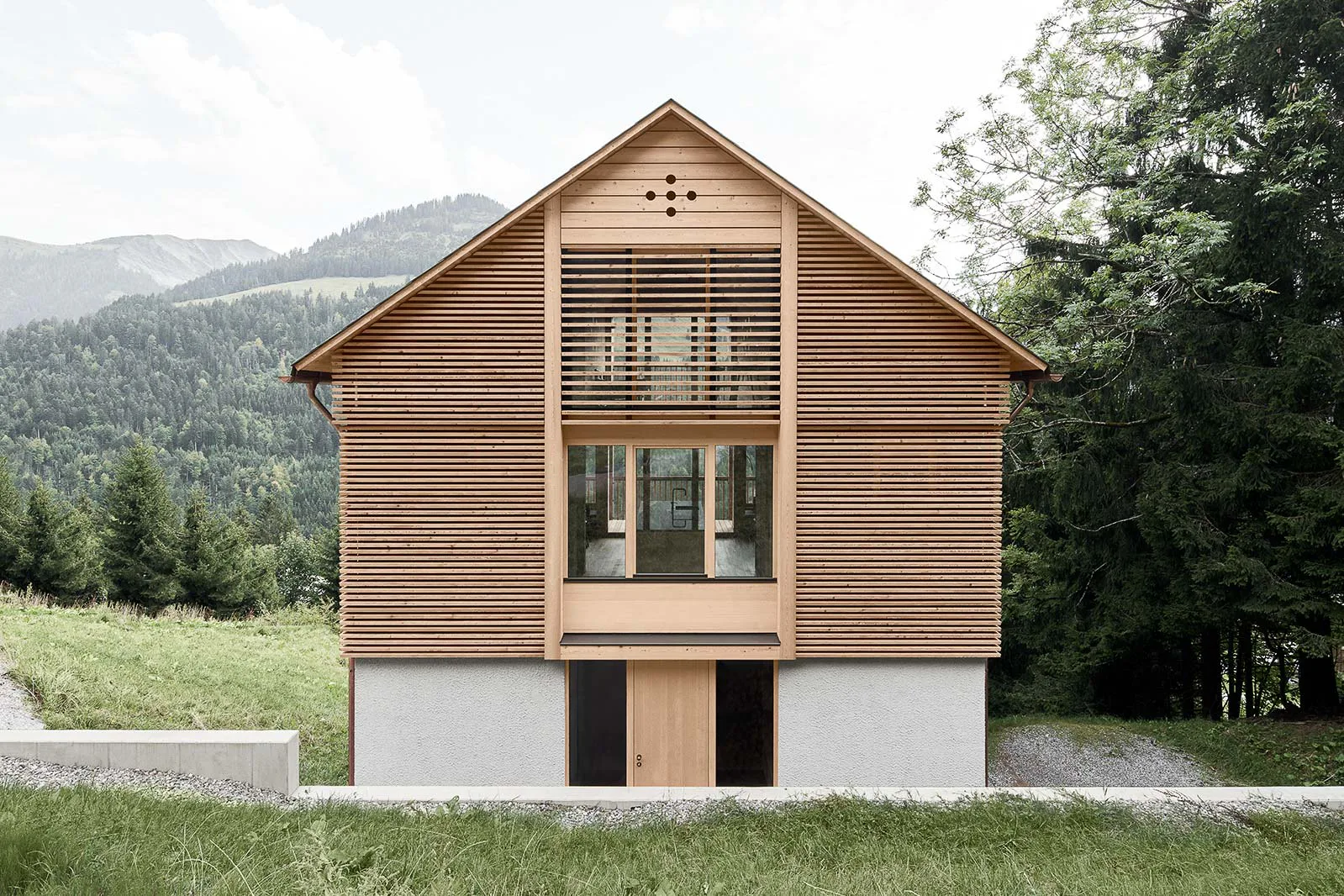 Auf dem massiven Betonsockel sitzt der hölzerne Aufbau inmitten der grünen Berglandschaft des Bregenzerwaldgebirges.