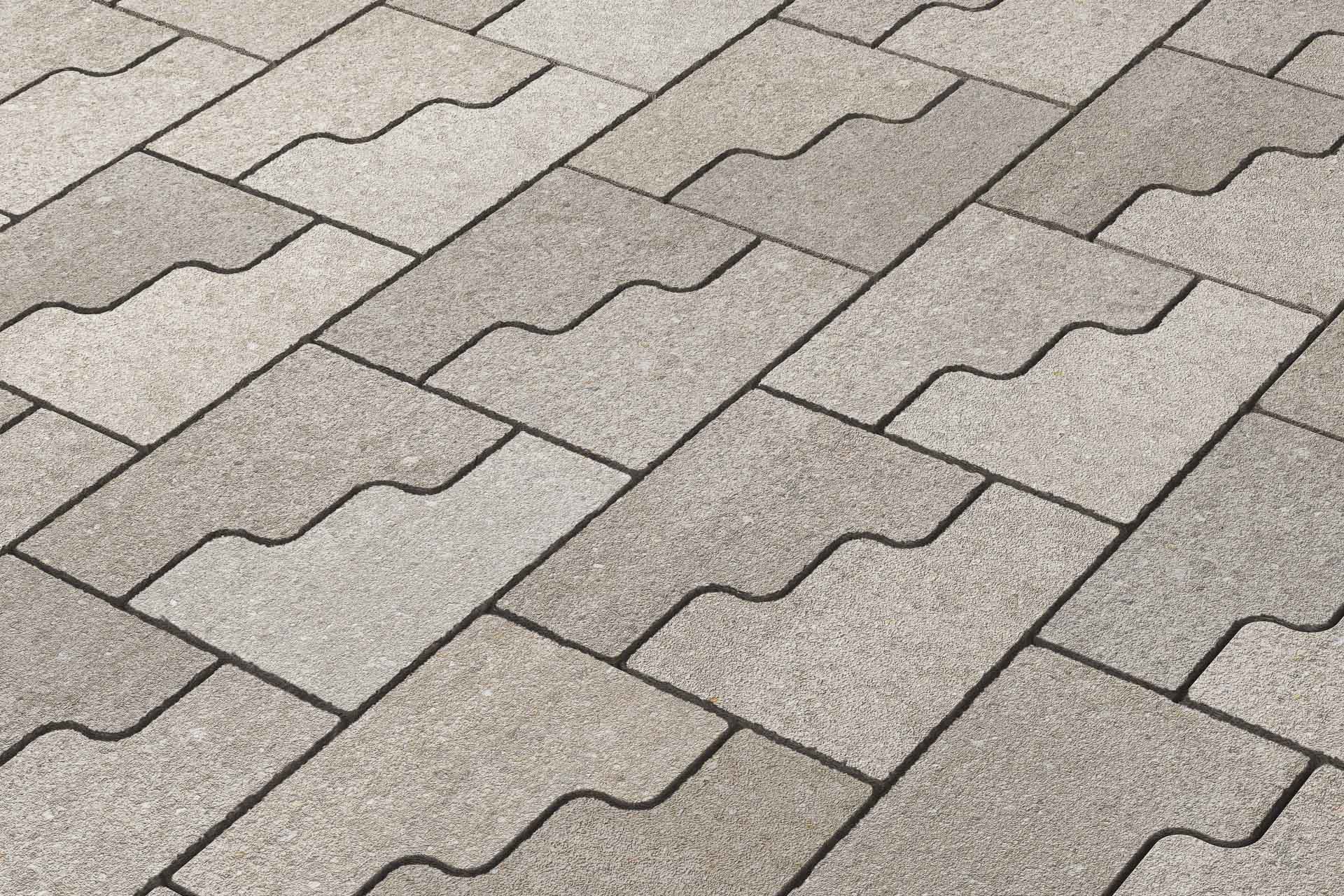 Zweiteilige Pflastersteine mit ineinandergreifender Geometrie bilden ein fließendes Fugenbild.