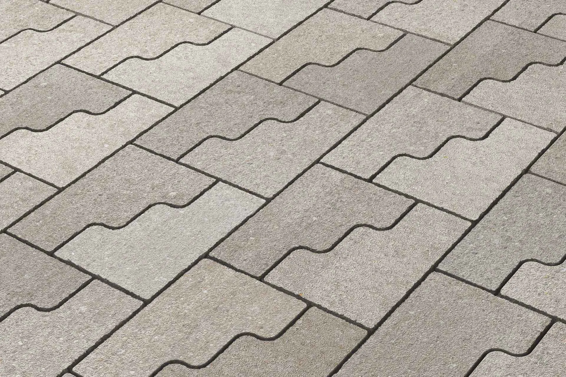 Zweiteilige Pflastersteine mit ineinandergreifender Geometrie bilden ein fließendes Fugenbild.