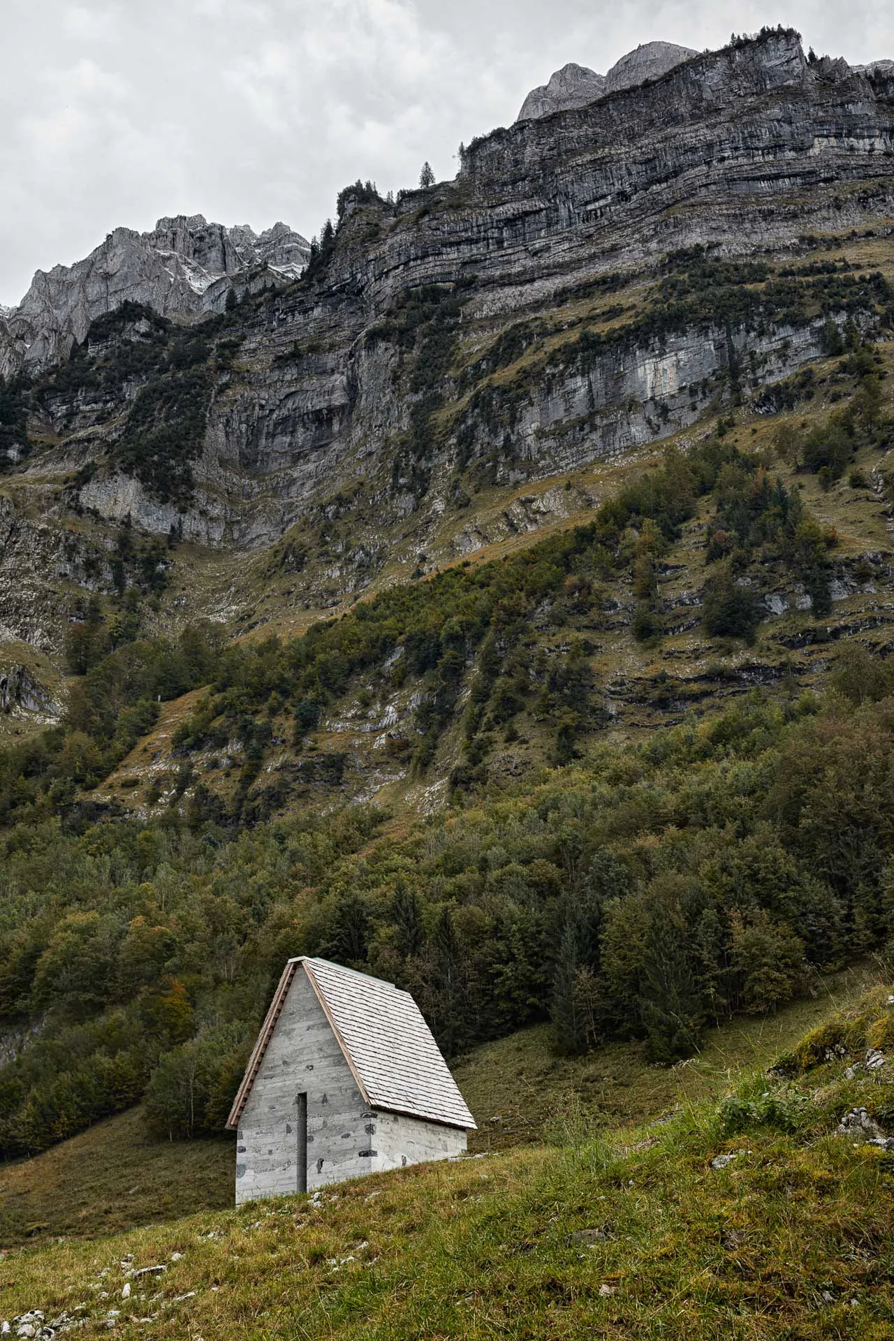 Am Fuße eines Berges schaffen Innauer Matt Architekten gemeinsam mit der Vorsässgenossenschaft Wirmboden Schnepfau eine kleine Bergkapelle mit steilem Giebeldach.