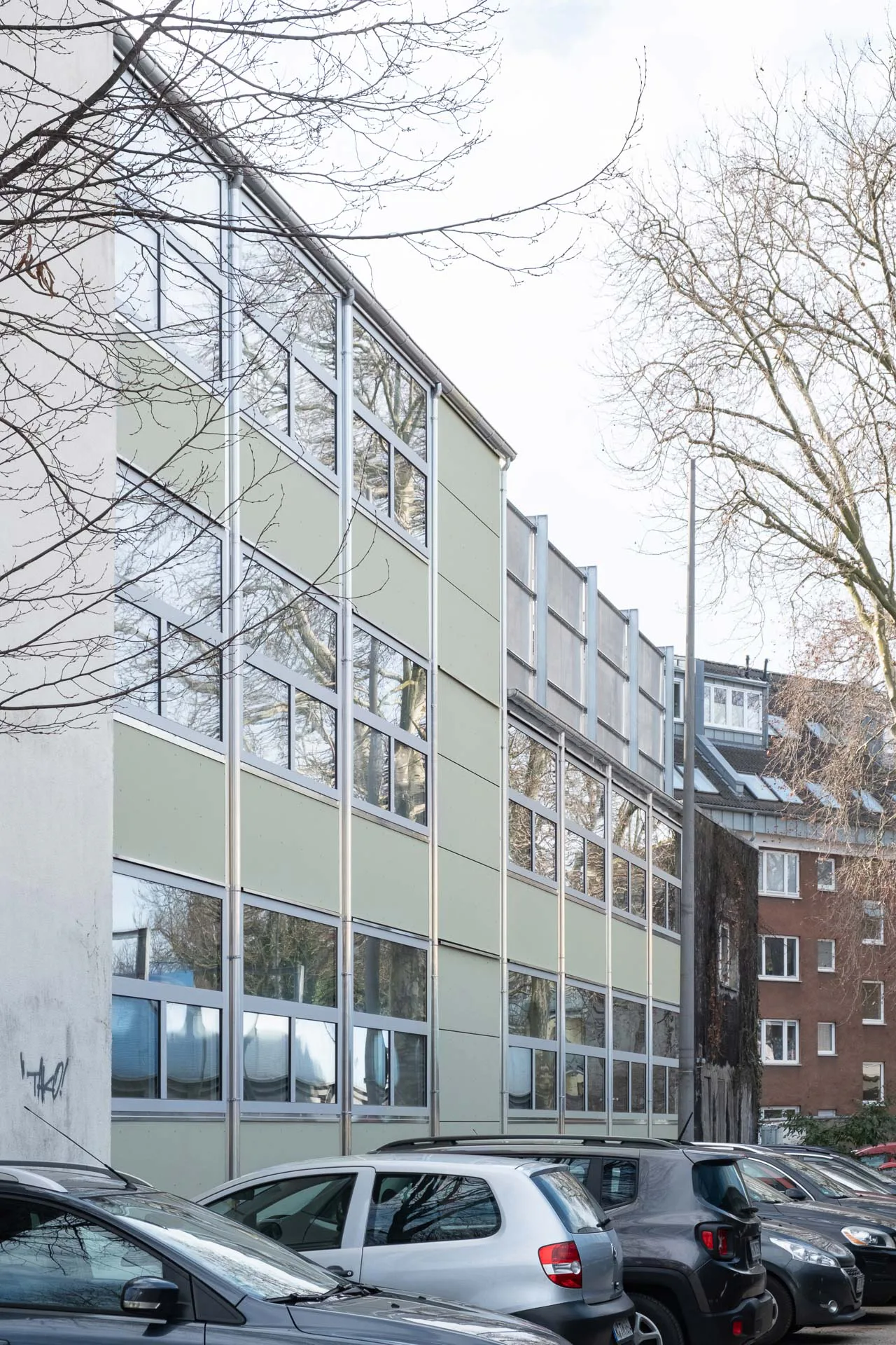 Die schräge Straßenfassade unterscheidet sich stark von der Hoffassade. Grüne Faserzementplatten verkleiden hier die geschlossenen Bereiche.