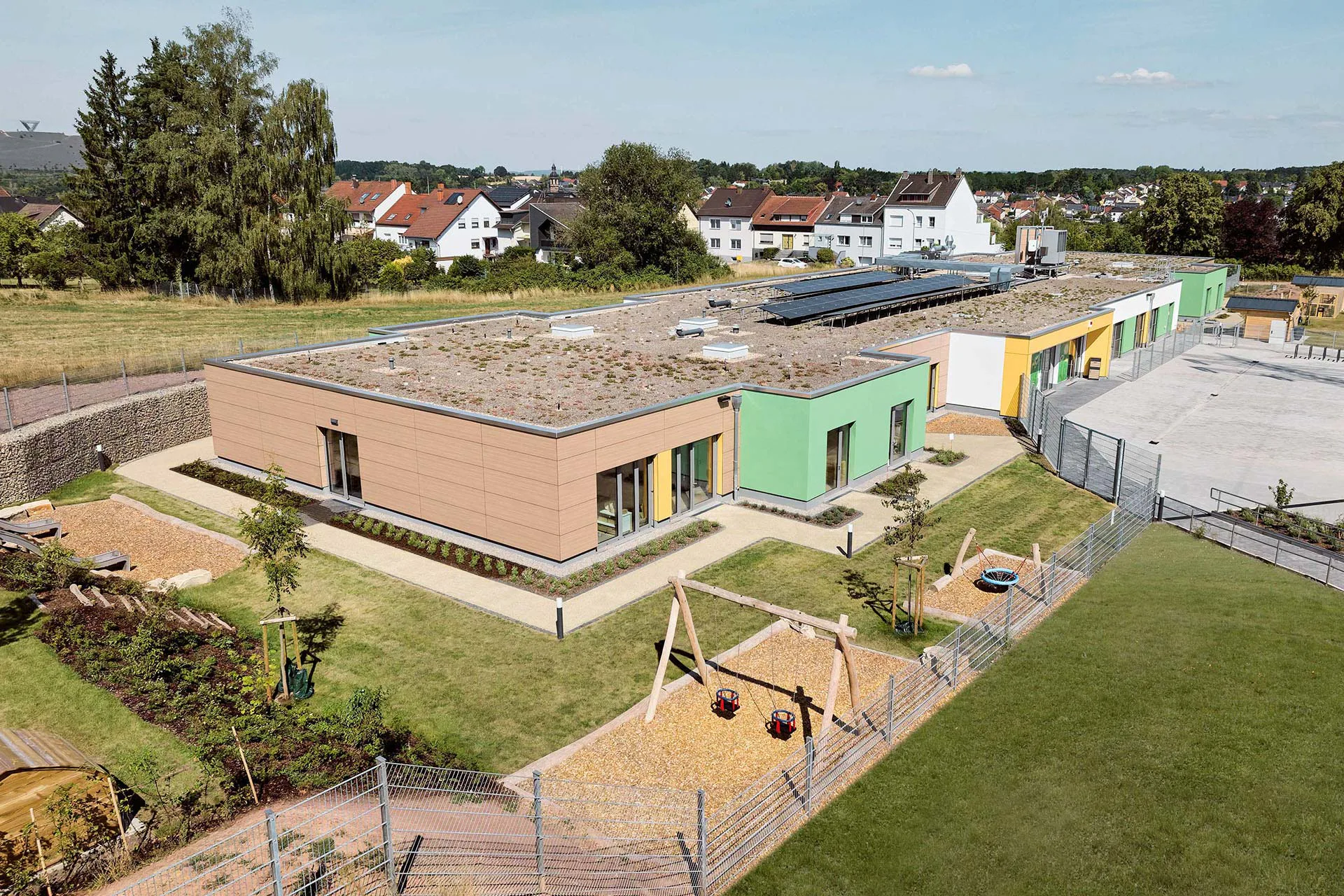 Der eingeschossige Neubau fügt sich in die Hanglage von Schwalbach-Hülzweiler ein. 32 Raummodule bilden acht Krippengruppen mit insgesamt 88 Plätzen.