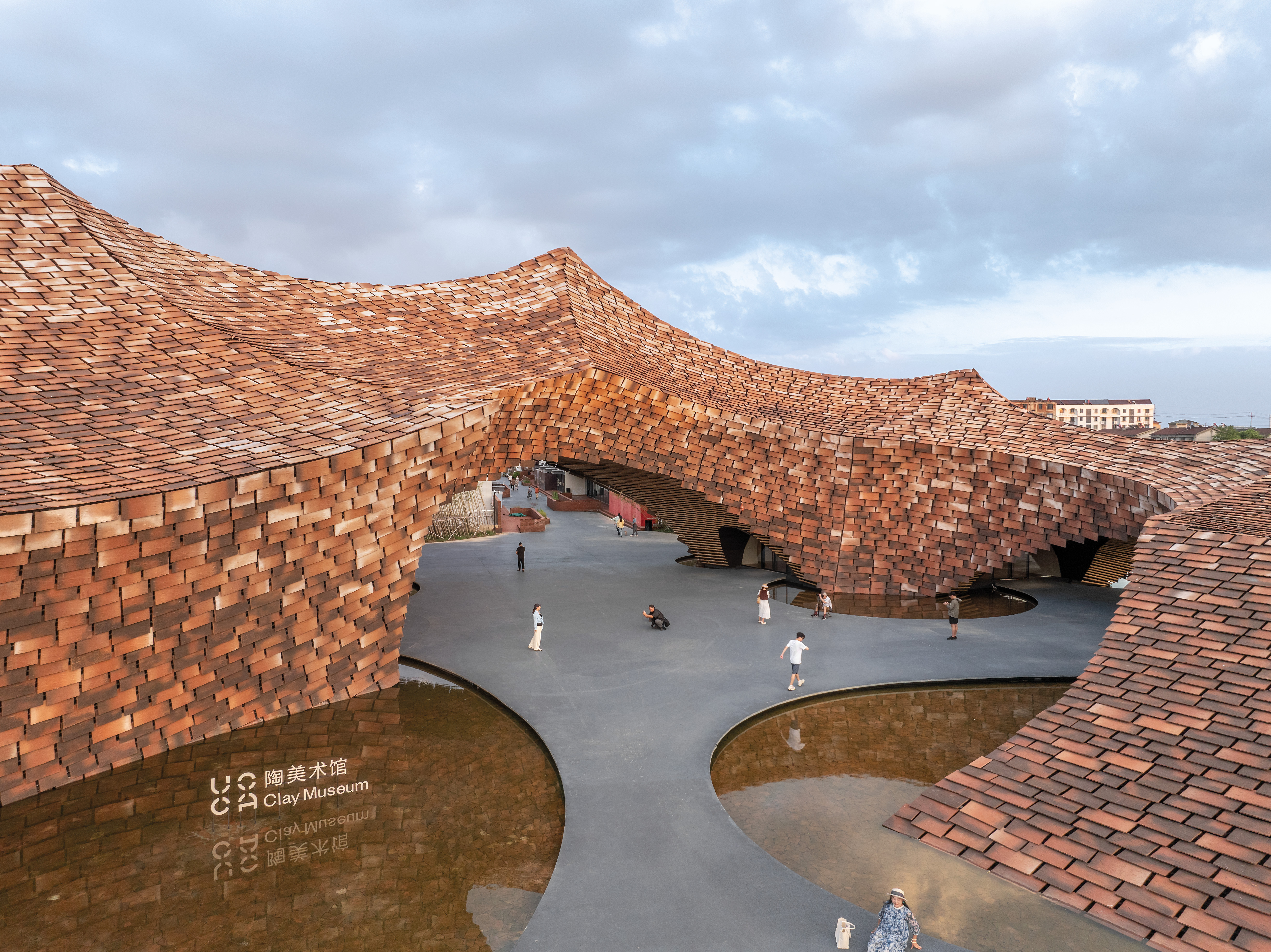 Resembling a bridge, the scaly armour of the UCCA Clay Museum spans across the passageways to the neighbouring buildings. Where this structure touches the ground, Kengo Kuma & Associates arranged shallow water basins.