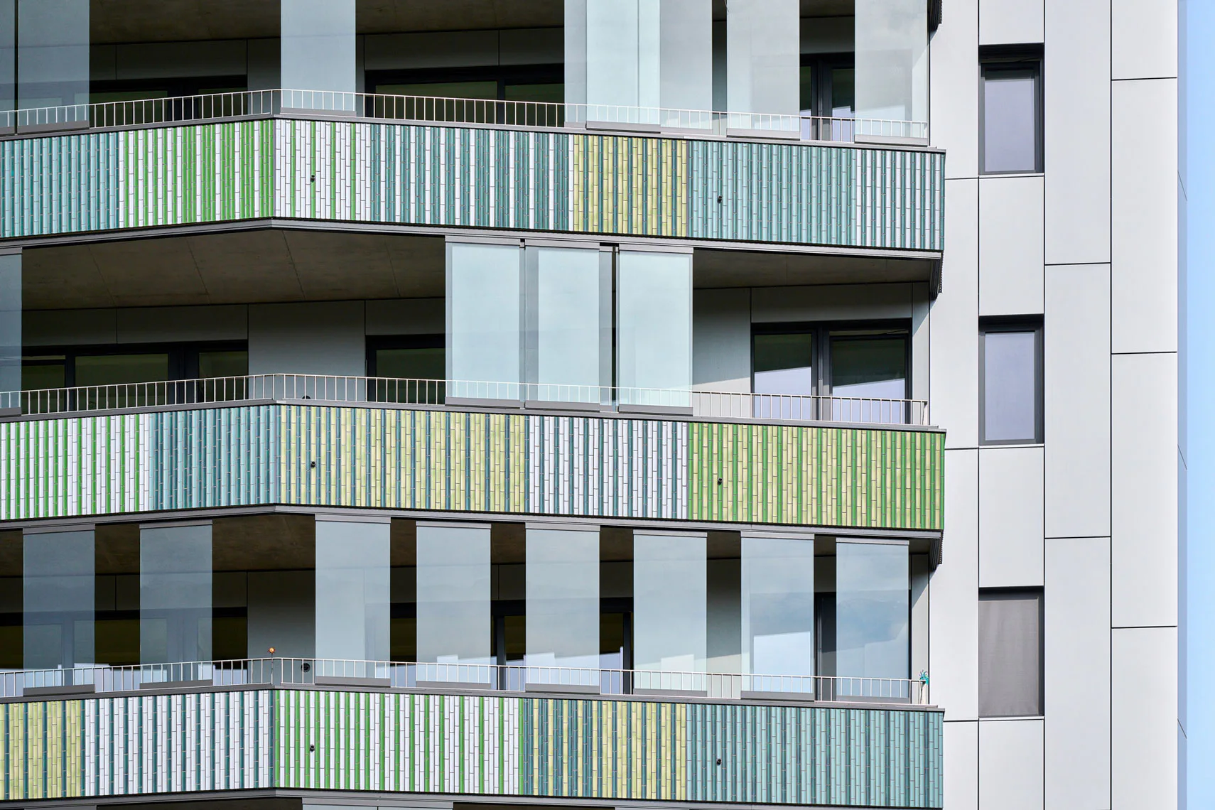 Verstärkt wird die Lebendigkeit der Fassade durch die sich immer wieder verändernde Position der Ganzglas-Schiebeelemente, mit denen die Balkone vor Wind und Wetter geschützt sind.